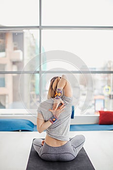 Woman practicing yoga, sitting in Cow Face exercise, Gomukasana pose, indoor interior background