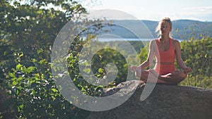 Woman is practicing yoga sitting lotus pose, at a beautiful exotic place on the top of a mountain at sunset. Meditation
