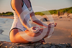 Woman is practicing yoga sitting in Lotus pose at sunrise. Silhouette of woman meditating on the beach