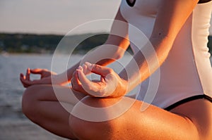 Woman is practicing yoga sitting in Lotus pose at sunrise. Silhouette of woman meditating on the beach