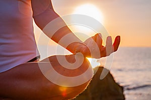 Woman is practicing yoga sitting in Lotus pose at sunrise. Silhouette of woman meditating at sunset on the beach