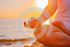 Woman is practicing yoga sitting in Lotus pose at sunrise. Silhouette of woman meditating at sunset on the beach