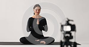 A woman practicing yoga sitting in the lotus position with namaste records a video lesson, addresses her intended audience