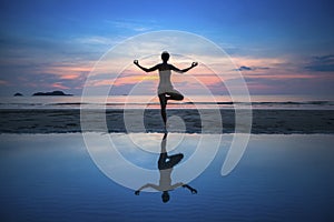 Woman practicing yoga during sunset at seaside.