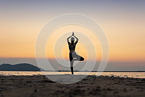 woman practicing yoga during surrealistic sunset at the seaside.