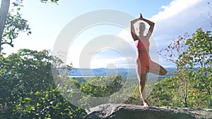 Woman is practicing a yoga in tree pose in a beautiful exotic place on the top of a mountain in the sunset