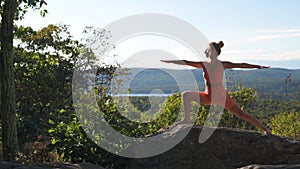 Woman is practicing yoga in warrior pose, at a beautiful exotic place on the top of a mountain at sunset. Harmony and meditation
