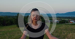 Woman practises yoga at sunrise under the tree. Young spiritual girl meditates in lotus pose nature outdoors, slow motion