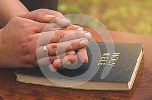 Woman praying on bible background. Hands folded in prayer concept for faith, spirituality and religion.