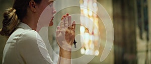 Woman praying in church. Sincerely believing adult girl worships God in cathedral. Folded hands with a cross.