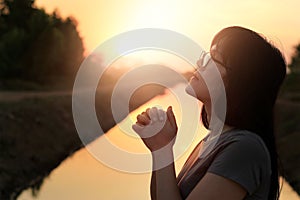 Woman praying with hands together on nature sunset