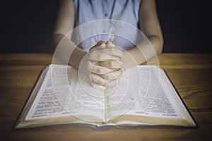 Woman praying with her hands over the bible.
