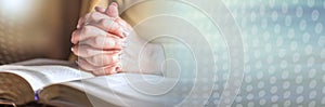 Woman praying with her hands over the bible, hard light; panoramic banner