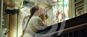 Woman praying on her knees in cathedral church. A sincerely believing girl prays to God.