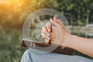 Woman praying on nature background.Hands folded in prayer on a Holy Bible for faith, spirituality and religion