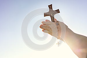 Woman praying outdoor with a crucifix with blinding sun light .