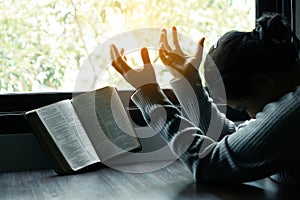 Woman prays by a window, embracing devotion and reflecting on her spiritual beliefs. The gentle light and tranquil ambiance create