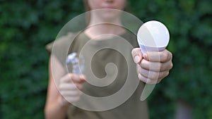 Woman preferring LED lamp to light bulb, saving natural resources, environment