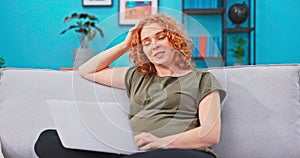 Woman in pregnancy, sitting at home on couch relaxing, talking through laptop camera with her