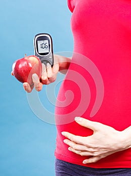 Woman in pregnant holding apple and glucometer with result sugar level, concept of diabetes during pregnancy