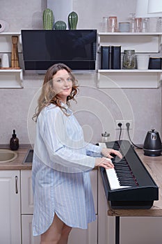 Woman pregnant musician stands in the home kitchen near the digital piano