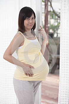 Woman pregnant standing beside home door and looking to camera