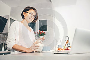 Woman prepare breakfast and watch a news in laptop