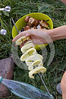 A woman prepares a barbecue of chicken and vegetables. Strung on a skewer a sweet