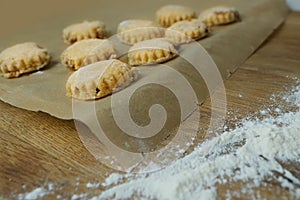 Woman prepares butter cookies at home in the kitchen, the table is sprinkled with flour, rolls out the dough, cuts out the shape,