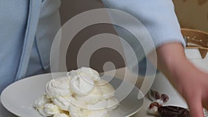 A woman prepares a cake Count ruins from meringue. Folds meringues on a plate, smeared with cream. Close-up