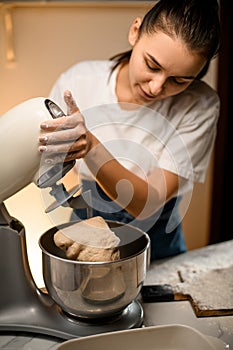 Woman prepares dough for bread using modern electric kitchen stand mixer.