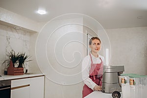 Woman prepares dough using kitchen mixer, pouring ingredients into steel bowl. Cooking homemade cake. Modern kitchen