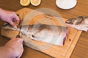 A woman prepares fish, cutting fish on a wooden board, the cook season the trout.