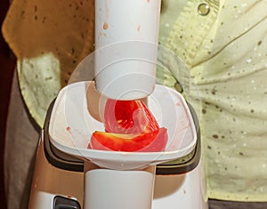 A woman prepares fresh healthy juice from tomatoes. Juicer at work. Diet concept for a healthy lifestyle