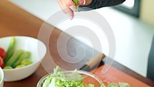 Woman prepares fresh salad with lettuce, tomatoes, and lime on wooden table