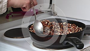 A woman prepares kozinak from nuts. Roasts sunflower seeds, peanuts and walnuts in a pan. In sugar and honey. Medium plan