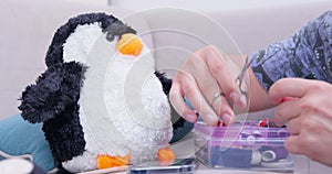 Woman prepares sewing accessories to fix torn plush penguin