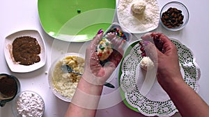 A woman prepares sweets from condensed milk, coconut shavings and almonds. Decorates sweets with colored glaze.