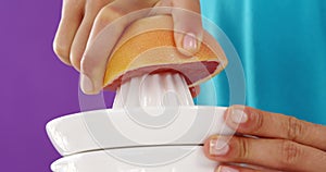 Woman preparing blood orange juice from juicer against violet background