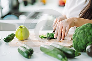 Woman preparing food in her kitchen. Female chopping fresh green vegetables on cutting board in light kitchen. Healthy