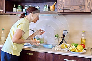 Woman preparing food in kitchen looking at recipe video on smartphone, talking online