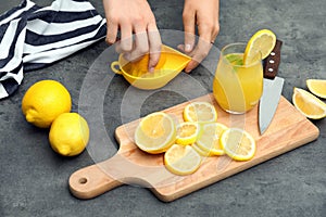 Woman preparing fresh lemon juice on grey table