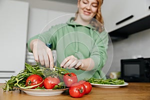 Woman preparing fresh vegetable salad in the kitchen with modern interior. Focus in the foreground.