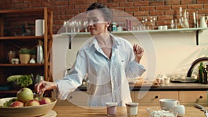 Woman preparing healthy breakfast. Girl putting two yogurt cups on wooden table.