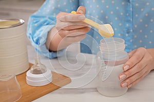 Woman preparing infant formula at table indoors, closeup. Baby milk