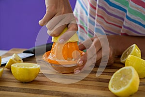 Woman preparing lemon juice from juicer against violet background