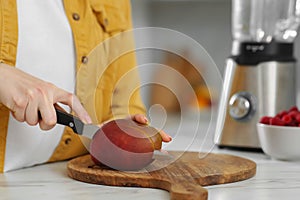 Woman preparing mango for tasty smoothie at white marble table in kitchen, closeup