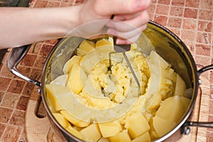 Woman preparing mashed potatoes with stainless potato masher. Cooking process, of mashed potato