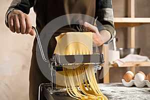 Woman preparing noodles with pasta maker machine at table indoors