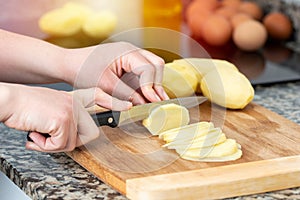 Woman preparing sliced potatoes on a wooden board